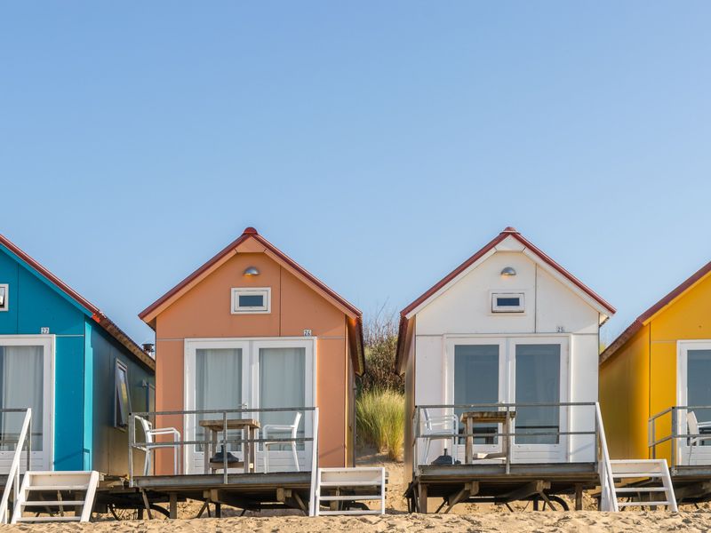 Cabanes de plage colorées alignées sur le sable, sous un ciel bleu