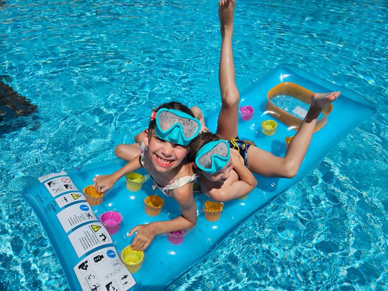 Deux enfants rieurs, masques de plongée sur le front, sur un matelas gonflable dans une piscine