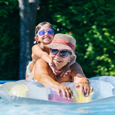 Une grand-mère et sa petite-fille allongées sur une bouée dans la piscine, lunettes de soleil sur le nez